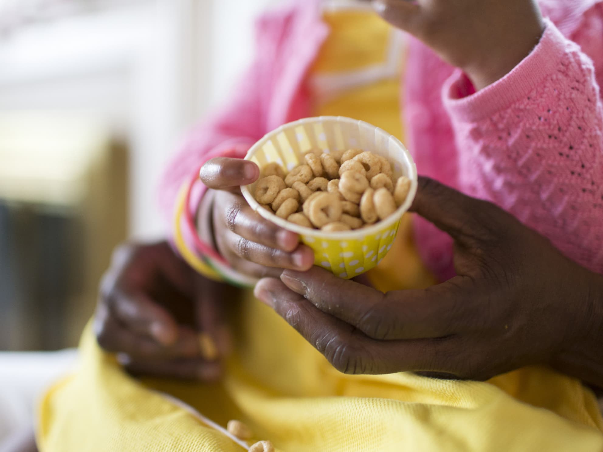 Child on mothers lap holding cup of Cheerios